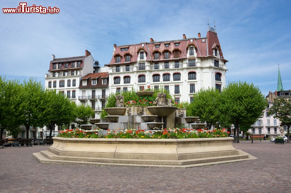 Immagine Un elegante palazzo di Aix-les-Bains, Francia, con una fontana abbellita da fiori e statue in primo piano.