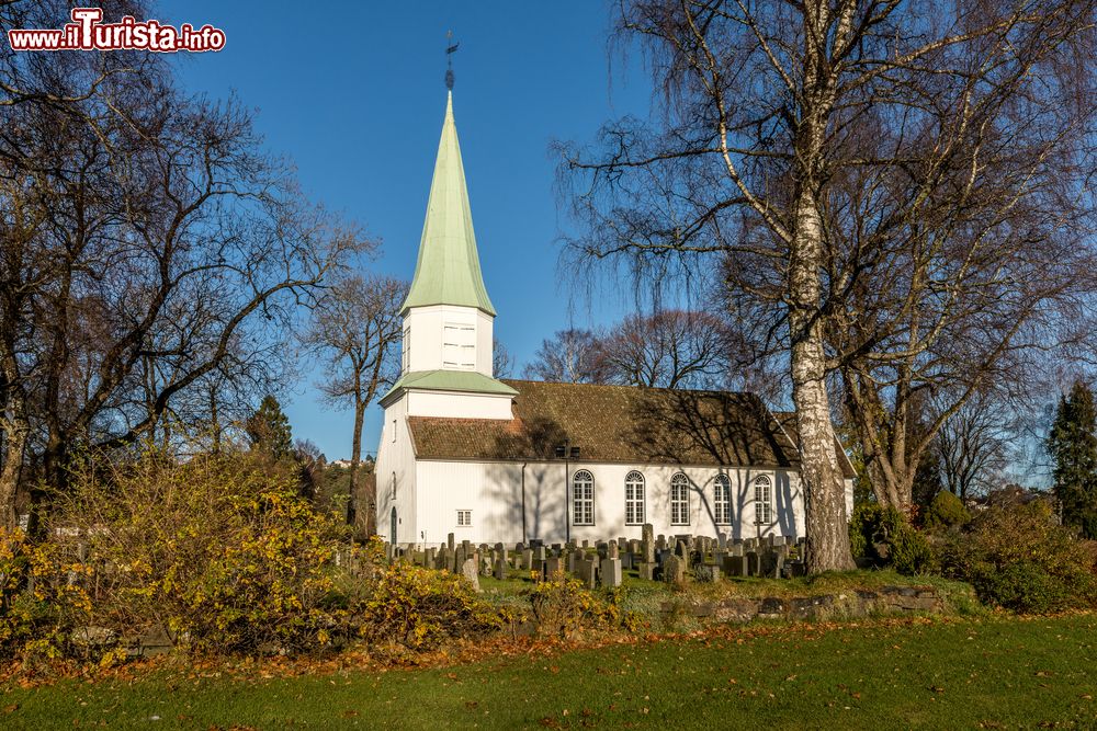 Immagine Una chiesa di legno fotografata a Kristiansand in autunno, Norvegia. Immerso nella vegetazione, l'edificio religioso è affiancato da un piccolo cimitero antico.