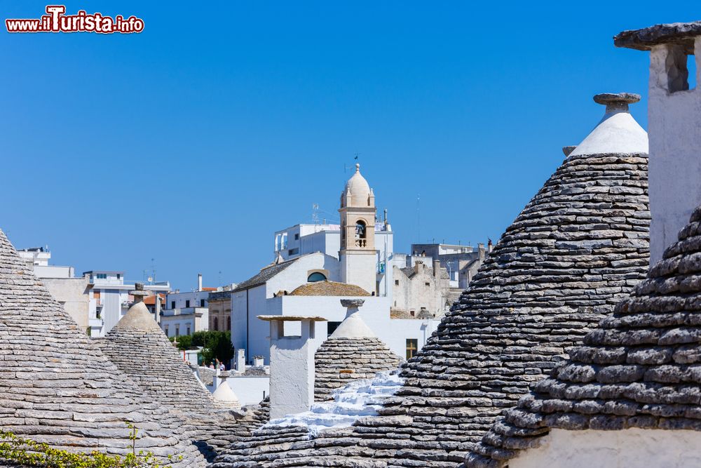 Immagine Una chiesa fra i tetti dei trulli di Alberobello, Puglia. Questa cittadina della provincia di Bari è celebre per le costruzioni coniche in pietra presenti a centinaia nel quartiere Rione Monti.