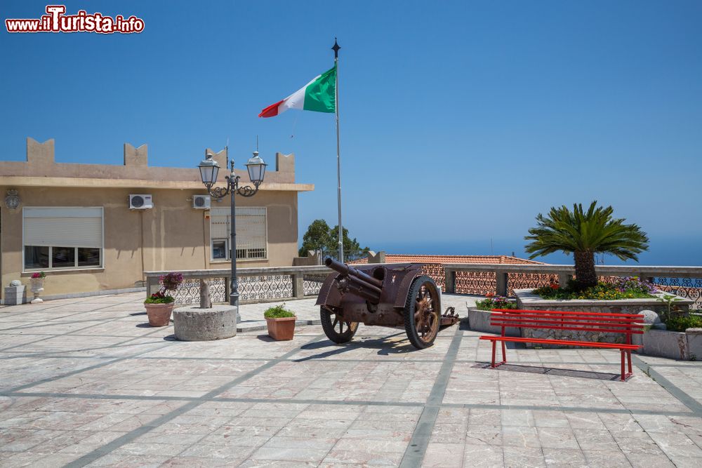 Immagine Una piazzetta di Forza d'Agrò, provincia di Messina, con un vecchio cannone e la bandiera italiana che sventola.