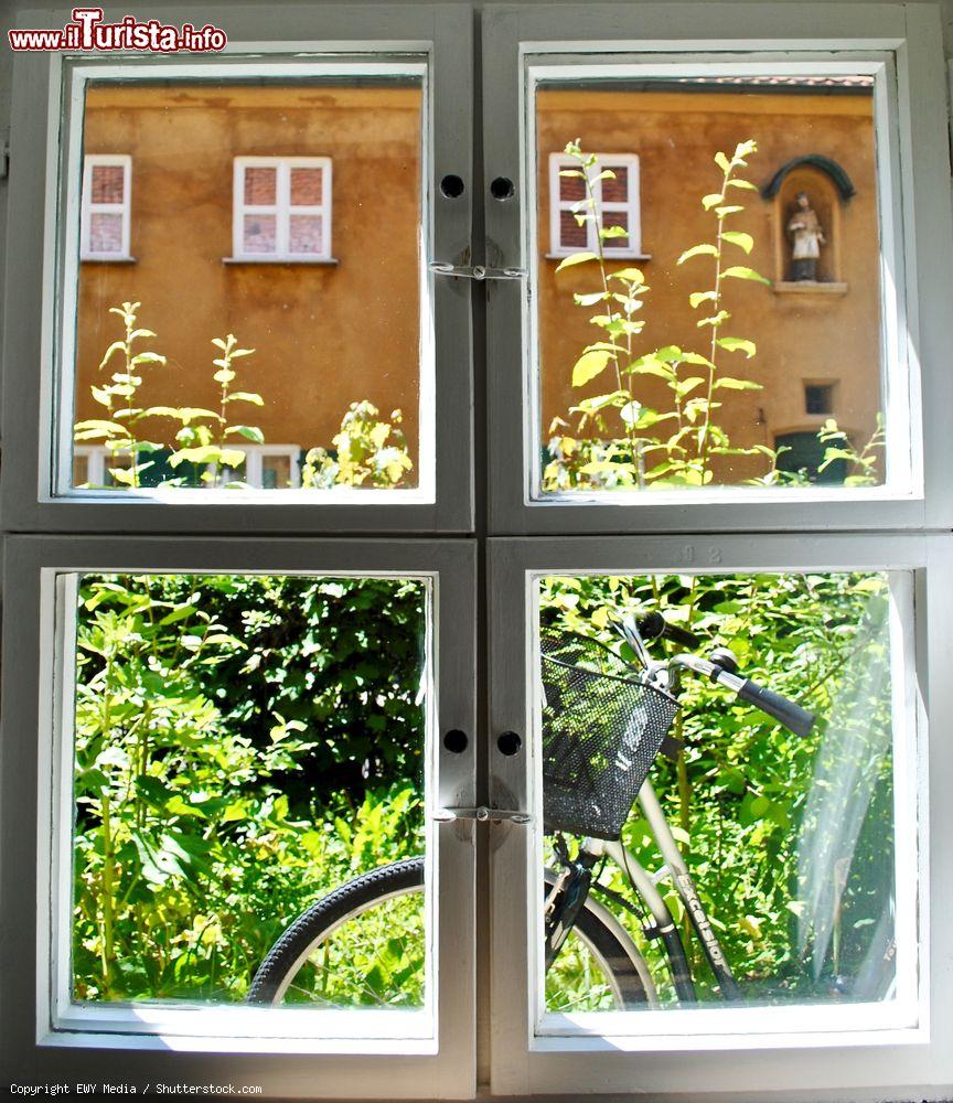 Immagine Veduta di un giardino con bicicletta al Fuggerei di Augusta, Germania, attraverso una finestra. Ancora oggi, come un tempo, i cancelli di questo antico complesso vengono chiusi alle 22 - © EWY Media / Shutterstock.com