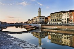 Case residenziali lungo il fiume Arno nel centro di Pisa, Toscana. Sullo sfondo la torre dell'orologio che si rispecchia nelle acque del fiume.


