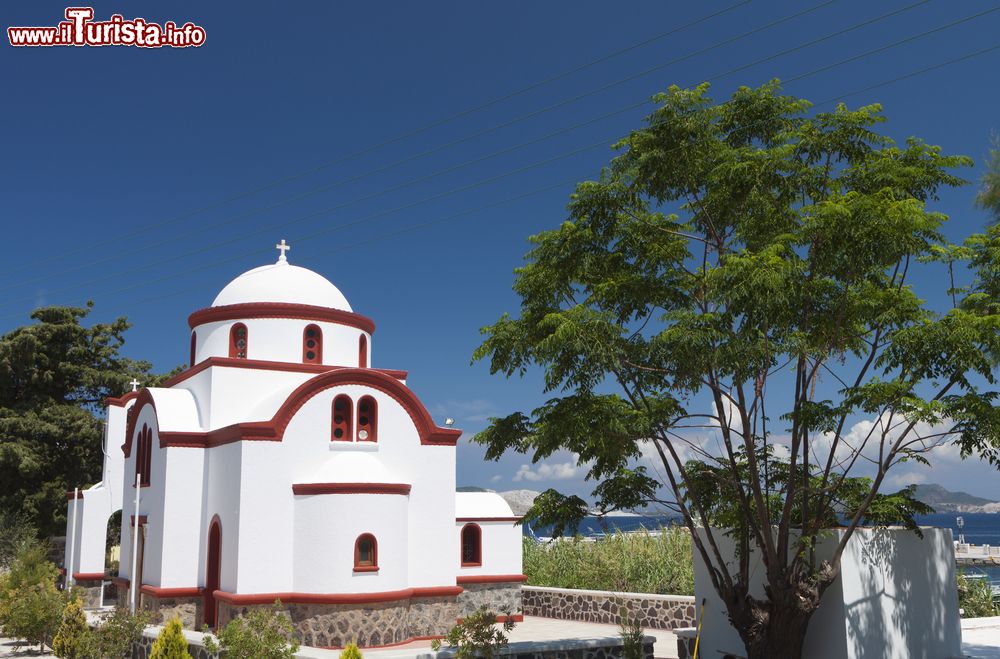 Immagine Una tradizionale chiesa greca a Mandraki, isola di Nisyros, Grecia, immersa nella vegetazione.