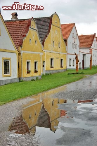 Passeggiando lungo la piazza centrale di Holasovice le facciate delle case si riflettono sulle pozzanghere