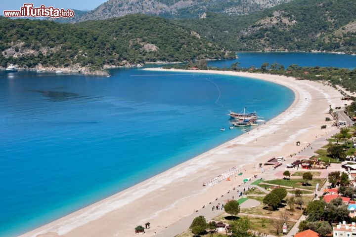 La Baia di Oludeniz nei pressi di Fethiye, in Turchia - Il nome Ölüdeniz, in turco, vuole dire “mare morto”. Probabilmente perché la porzione di mare che lambisce questa spiaggia – tra le più spettacolari e fotografate della Turchia – è quasi completamente chiusa, separata dal Mediterraneo da una lingua di terra lunga e sottile. Il risultato è una baia a forma di cuore, con il fondale basso e l’acqua calma, simile a un grande lago salato dalle sfumature verdi e turchesi. C’è chi l’ha ribattezzata “Laguna Blu”, e il soprannome è decisamente più appropriato. Dietro la spiaggia di Ölüdeniz si erge il monte Baba, e tutt’intorno il paesaggio è tappezzato da una fresca pineta che fa parte di un parco naturale. Ideale per i bambini, che possono divertirsi in tutta sicurezza, la baia offre agli adulti un paesaggio mozzafiato ma anche tante possibilità per svagarsi, tra sport acquatici, escursioni e il lancio col parapendio dalla vicina vetta del Baba. L’ingresso alla spiaggia è a pagamento (un paio di euro, con sconti per alcune categorie).
Ölüdeniz si trova sulla costa occidentale della Turchia, a 9 km circa da Fethiye, che è raggiungibile in navetta dall’aeroporto di Dalaman. Da Fethiye si può raggiungere la spiaggia in pullman - © NCG / Shutterstock.com